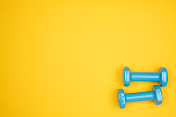 Wall Mural - Blue dumbbells on yellow background, top view with copy space