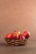 A vase of red apples on a uniform brown background. Wicker basket with seasonal harvest fruits