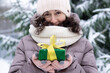 A beautiful middle-aged 45-year-old woman holding a nice Christmas present in the air. Snowy landscape with spruce and snow