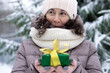 A beautiful middle-aged 45-year-old woman holding a nice Christmas present in the air. Snowy landscape with spruce and snow.