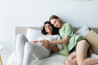 © LIGHTFIELD STUDIOS - happy woman touching belly of pleased pregnant girlfriend in bedroom