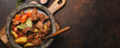 Delicious beef meat stew dish with potatoes, carrot and gravy in rustic metal bowl with spoon, bunch of fresh parsley, garlic cloves, spices on brown concrete background top view space for text