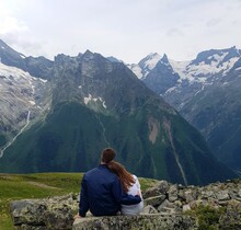 Rear View Of Couple Sitting On Rock Against Mountains