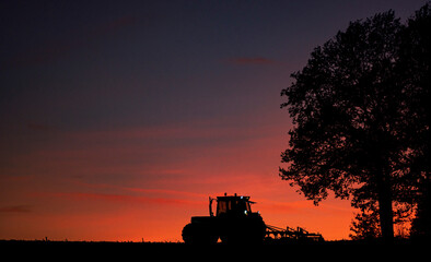 Traktor bereitet den Boden für die Bepflanzung  mit Sonnenuntergang und Himmel im Hintergrund