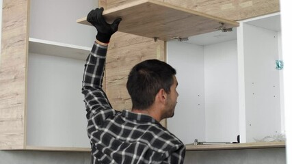 Wall Mural - The carpenter screwing in and mounting hinge on kitchen shelves.