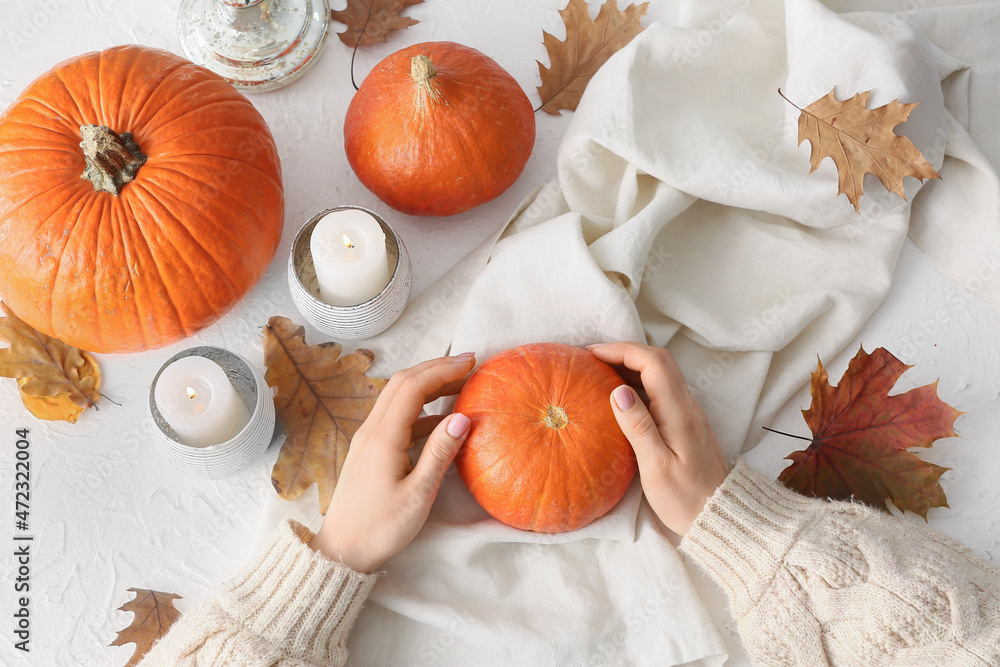 Woman with pumpkins and candles on light background