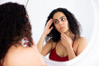 Portrait of young woman checking face skin in round mirror at home