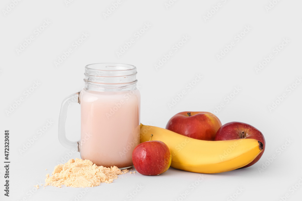 Mason jar with protein shake, powder, banana and apples on white background