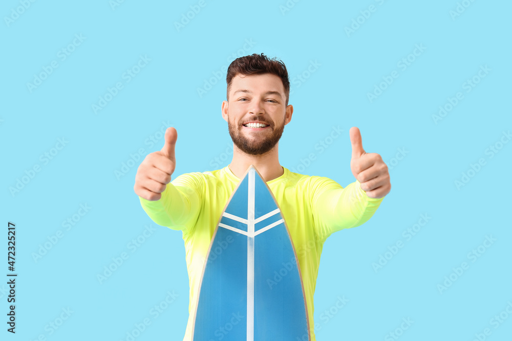 Handsome bearded man with surfboard showing thumbs-up on blue background