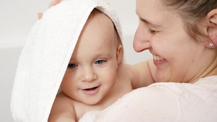 Wall Mural - Portrait of smiling young mother wiping wet hair and head of baby son after having bath. Concept of children hygiene, healthcare and family care at home