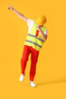 Young male worker dancing on yellow background