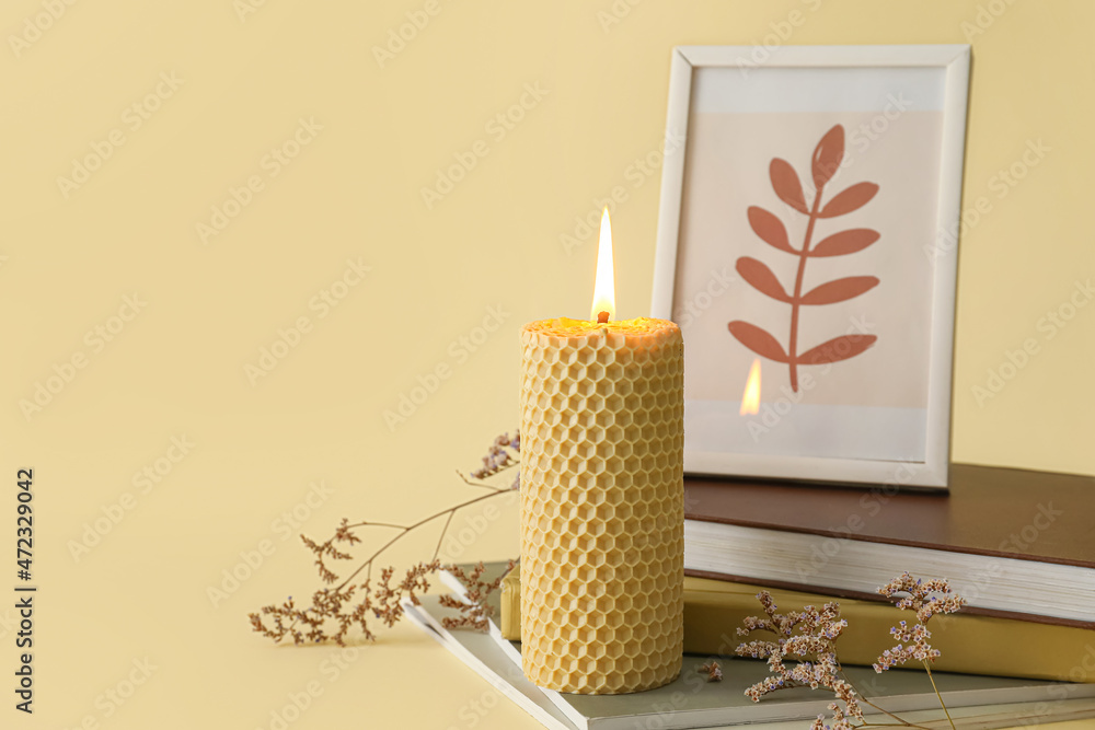 Composition with glowing candle and books on yellow background
