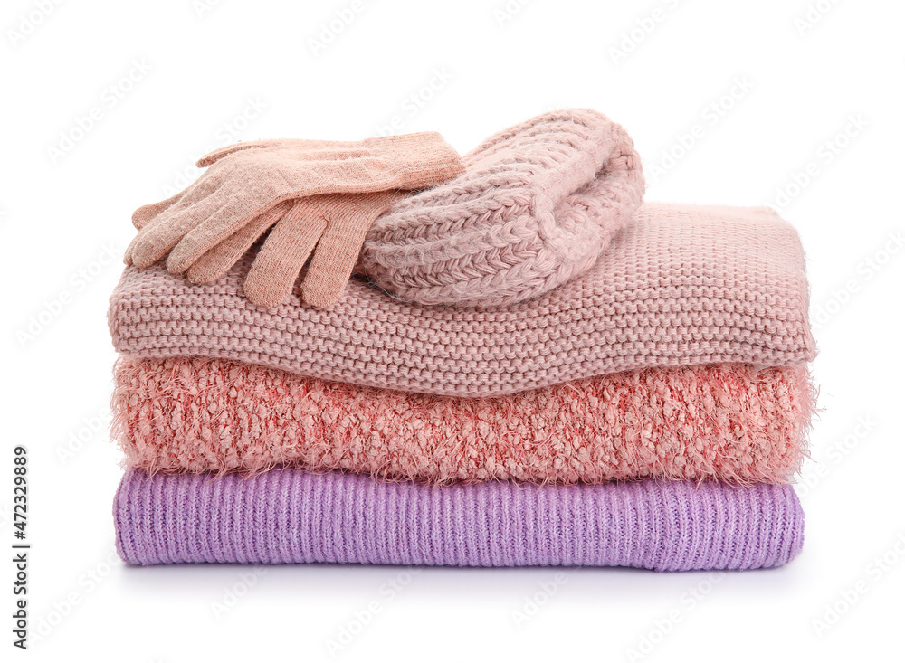 Stack of stylish sweaters, gloves and hat on white background