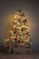 Beautiful Christmas tree with glowing lights, gifts and wooden reindeer near brick wall