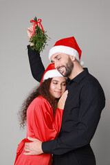 Poster - Lovely couple in Santa hats under mistletoe bunch on grey background