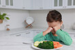 Cute little girl crying and refusing to eat vegetables in kitchen, space for text
