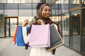 Arabic woman wearing hijab standing with shopping bags near mall