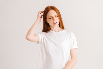 Wall Mural - Studio portrait of confused pretty young woman pondering over something touching head standing on white isolated background. Front view of redhead bewildered lady scratching head as seeks.