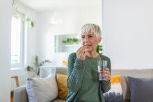 Senior Woman Takes Pill With Glass Of Water In Hand. Stressed Female Drinking Sedated Antidepressant Meds. Woman Feels Depressed, Taking Drugs. Medicines At Work