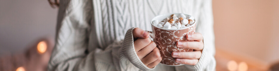 Wall Mural - Girl in a cozy knitted sweater drinking coffee from a mug