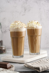 Two tall glasses with cold coffee drink frappe - iced cappuccino with whipped cream on a marble board