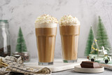 Two tall glasses with cold coffee drink frappe - iced cappuccino with whipped cream on a marble board and christmas ornaments and decoration