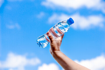  A girl holds a bottle of drinking water in her hand against a blue sky background
