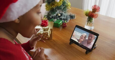 Wall Mural - African american woman with santa hat using tablet for christmas video call with couple on screen