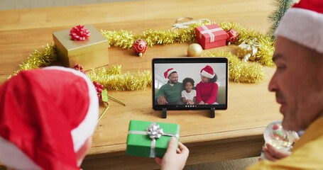 Canvas Print - Caucasian father and son with santa hats using tablet for christmas video call with family on screen