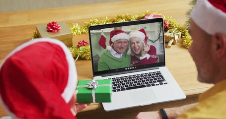 Canvas Print - Caucasian father and son with santa hats using laptop for christmas video call with couple on screen