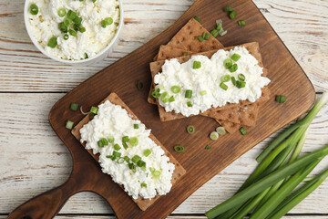 Crispy crackers with cottage cheese and green onion on white wooden table, flat lay