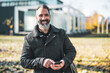 © djoronimo - Businessman is using smartphone in front of company building in park. Happy businessman in autumn.