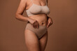 © Taras Grebinets - Close-up body of overweight woman with stretch marks and saggy belly after pregnancy, isolated on beige background with copy space for ads. Concept of love and acceptance, body positive.