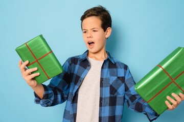 Wall Mural - Happy kid boy holding many present and gift boxes isolated over blue background.