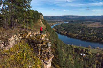 Wall Mural - A man stands on the edge of a cliff and admires the view of the river