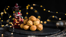 Cookies Nuts With Condensed Milk Against The Background Of New Year's Garlands. New Year's Sweets On A Dark Background. Homemade Pastries. Toy New Year's Deer.