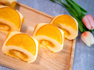 Wall Mural - Close up of orange cake roll with slice orange fruit on wooden plate.