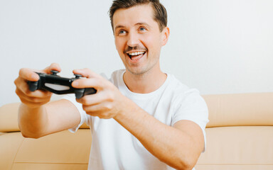 Wall Mural - Happy young man playing video game with joystick, enjoying active leisure while sitting on sofa at home. Joyful guy player gamer with gamepad and hobby electronic sport