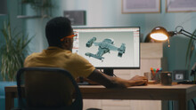 Back View Of Black Man In Yellow T Shirt And Glasses Creating 3D Model Of Modern Aircraft On Computer While Sitting At Table In Home Office And Working On Remote Project