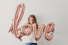 Smiling Girl Showing Love Balloon While Standing In Front Of Wall