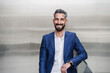 © Westend61 - Mid adult businessman smiling while leaning on railing in front of silver colored wall