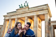 Man and woman bite into the typical German sweet, brezen, at the Brandenburg Gate.