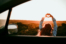 Woman Making Heart Shape With Hands Seen Through Car Window During Sunset