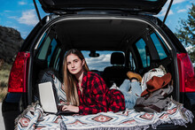 Female Freelancer Lying With Laptop In Car Trunk On Sunny Day