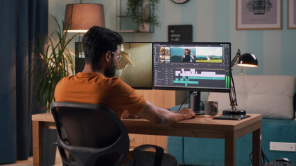 Wall Mural - unrecognizable man in orange t shirt using computer to edit video while sitting at table and working