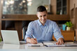 © amnaj - Businessman working on laptop and taking notes in office.