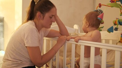 Wall Mural - Tired sleepy mother rocking crib of her baby crying and refusing to sleep at night. Concept of parenting, parent fatigue and children development.