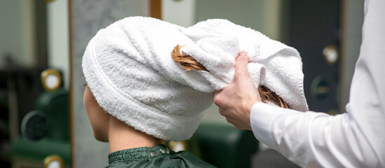 Wall Mural - A hairdresser is wrapping the wet hair of the young woman in a towel after washing at the beauty salon