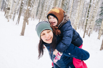 Young  mother and child girl on a winter walk in nature playing with snow. A girl on a sled with gifts on the eve of the new year in the park. Two sisters walk in a New Year's park