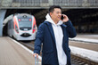 © Liubomir - Business man Asian man at the train station having fun talking on the phone, a passenger arrived on a business visit to a new city, with a large suitcase of luggage